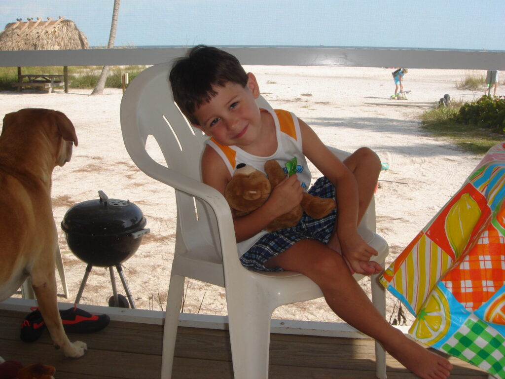 small boy with holding teddy bear with dog sitting nearby