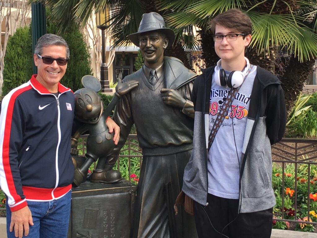 two men standing next to Walt Disney statue