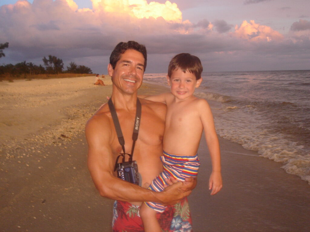 father holding son at beach sunset
